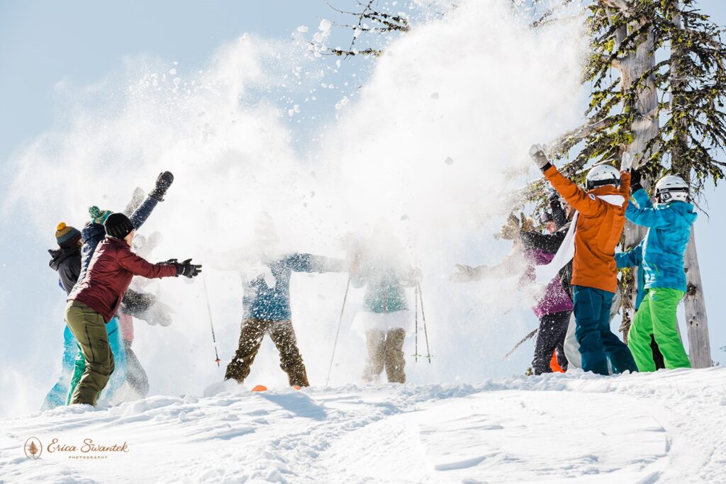 bride and groom skiing down the mountain at mt bachelor with friends throwing snow at them