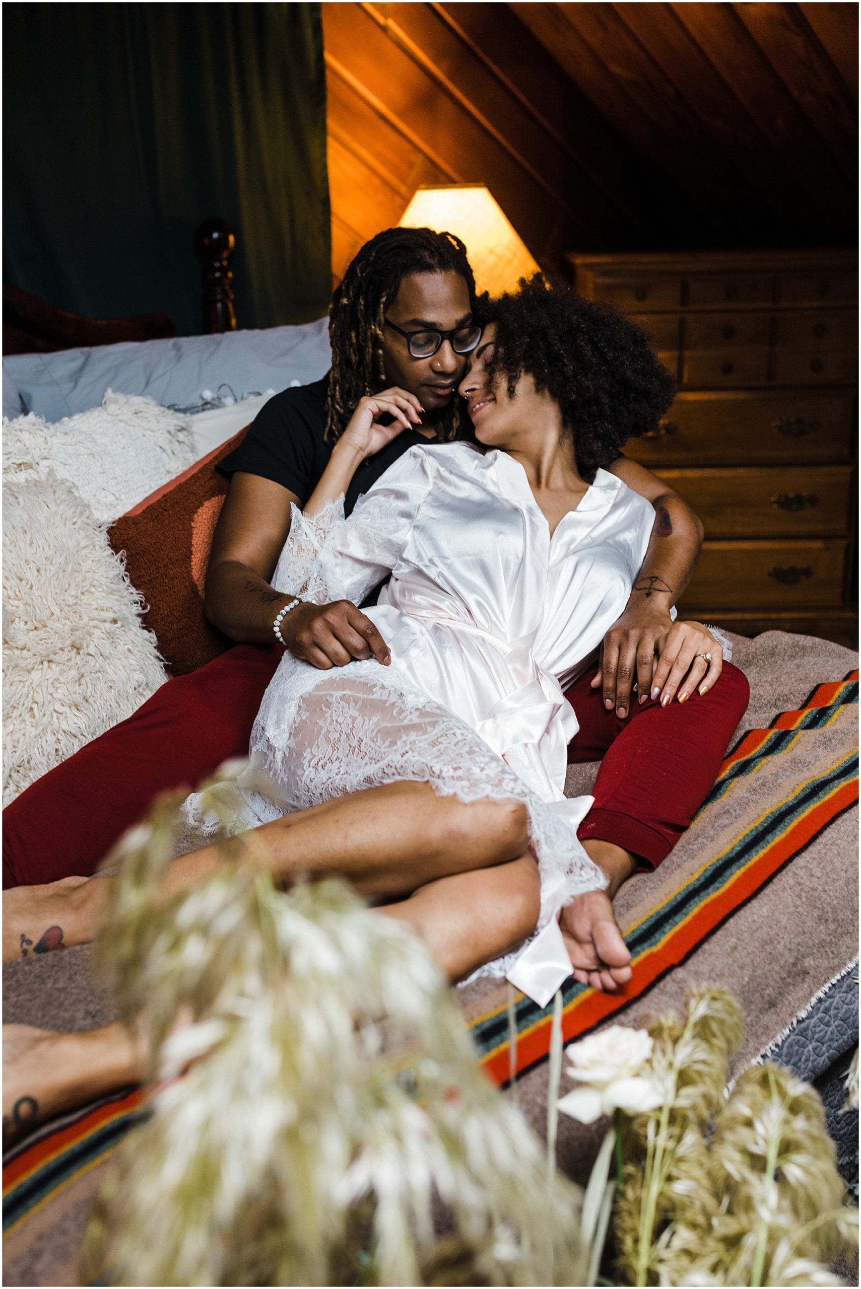 A young black woman wearing a white robe nestles into her man's arms as they spend the morning in bed before they marry on the beach in Oregon. | Erica Swantek Photography