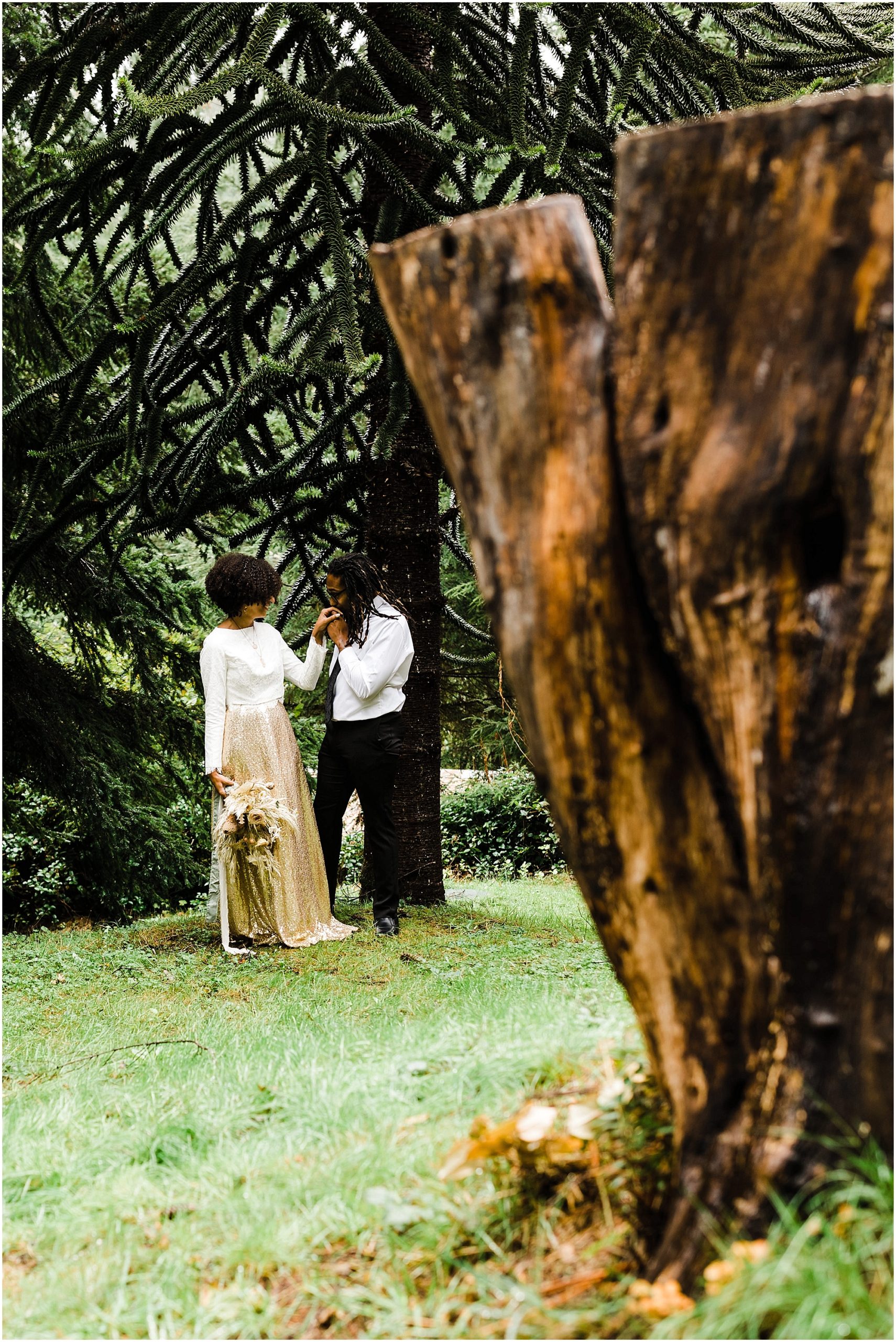 A black groom wearing a white shirt and black pants kisses his fiancées hand after seeing her in her gorgeous wedding attire before their Oregon Coast elopement. | Erica Swantek Photography