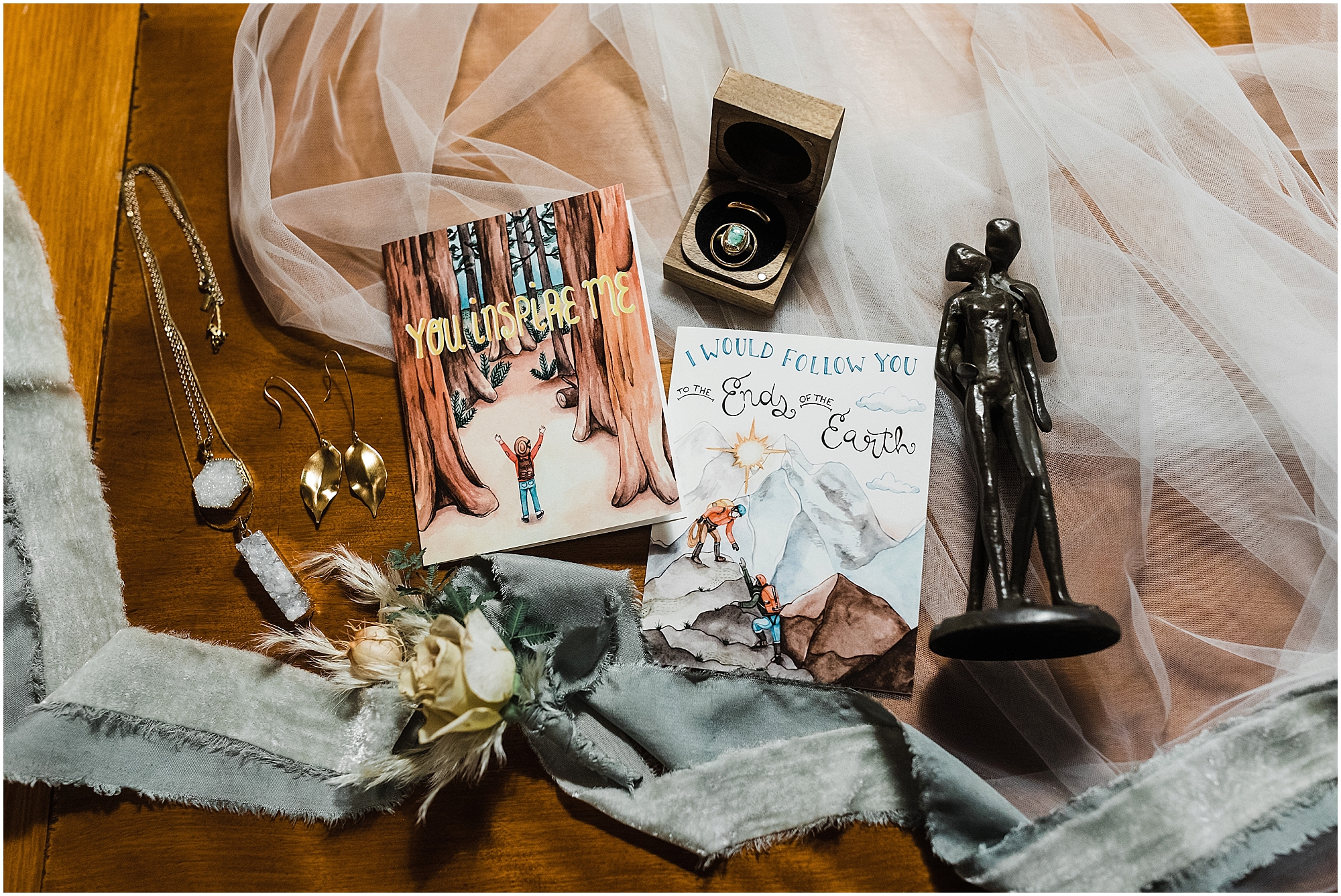 A detailed flat lay featuring handmade jewelry, artwork, vow cards, wedding rings, a veil and silk ribbon for this earthy Oregon Coast elopement. | Erica Swantek Photography