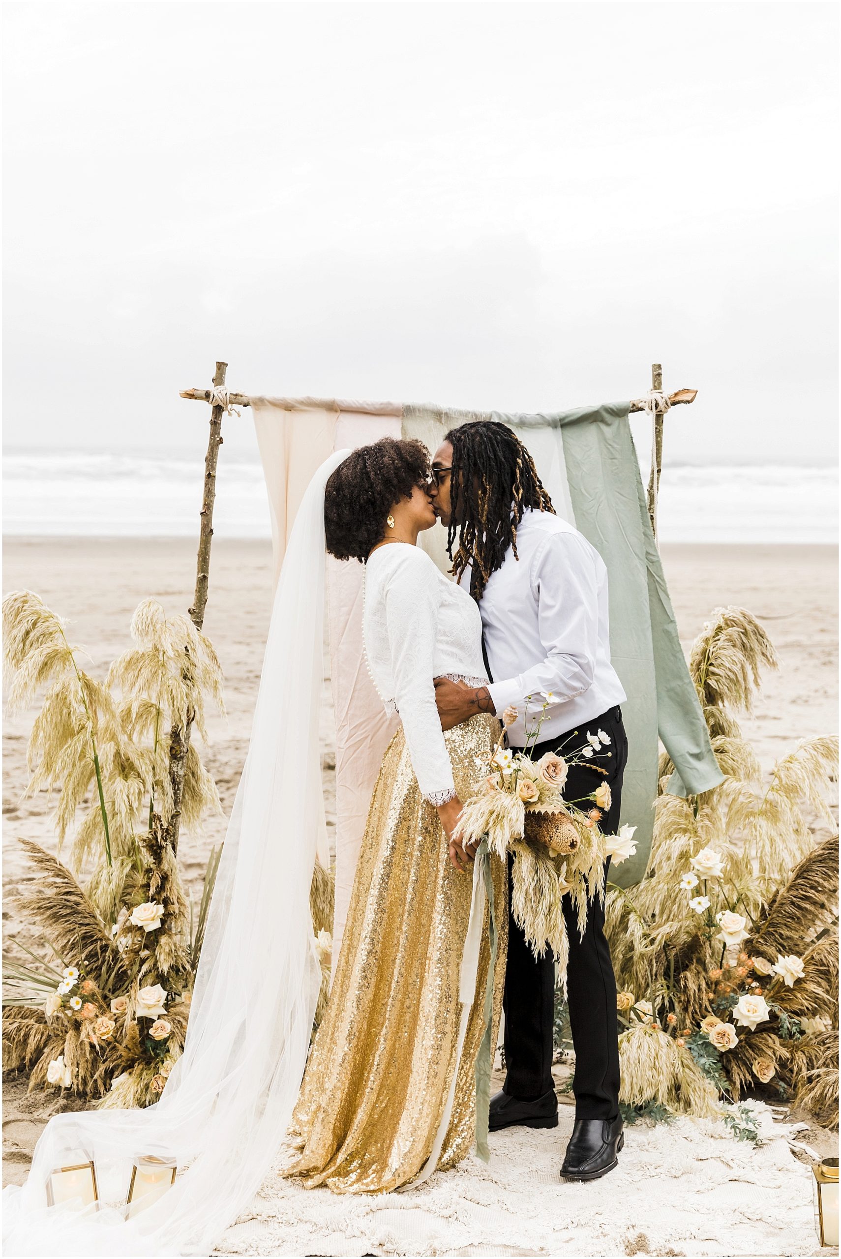 A gorgeous couple kisses in front of their outdoor beach alter made of rustic logs, silk ribbon and framed with beautiful florals in a neutral color palette for their romantic Oregon Coast elopement. | Erica Swantek Photography