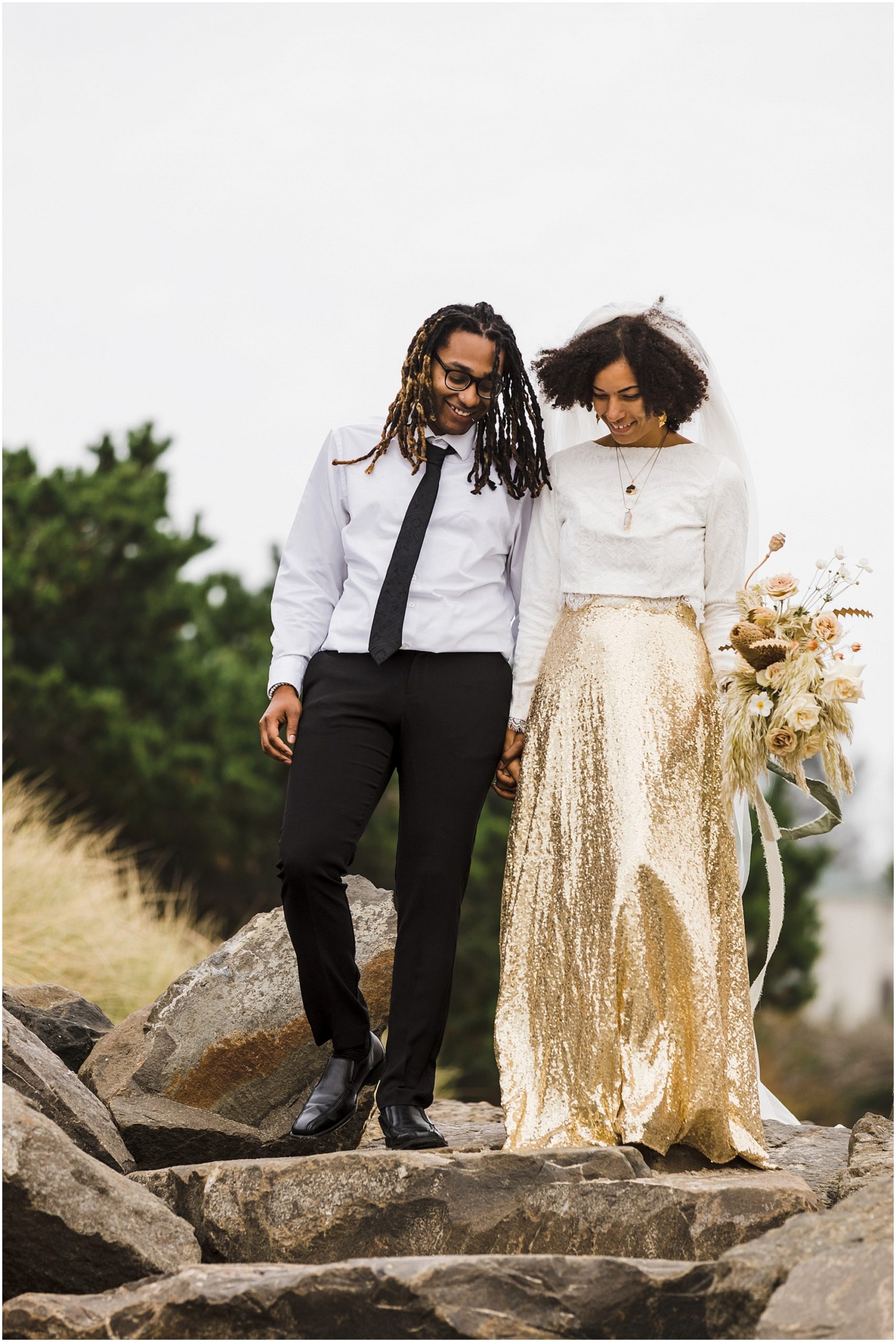 A gorgeous black couple walks down the rock staircase holding hands as they get ready to say their vows on their epic Oregon Coast elopement day. | Erica Swantek Photography