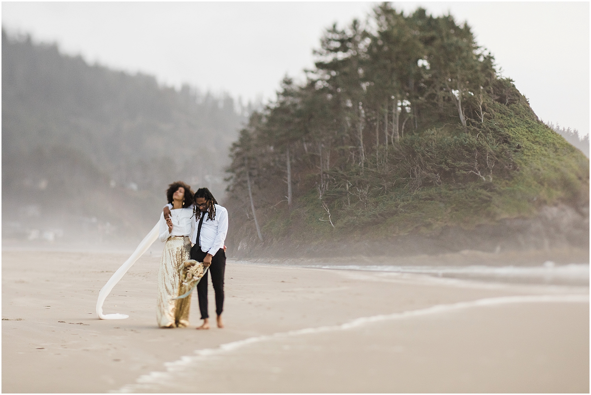 A BIPOC couple walks along the shoreline of the Pacific Ocean with their arms around each other, reflecting on their epic Oregon Coast elopement day. | Erica Swantek Photography