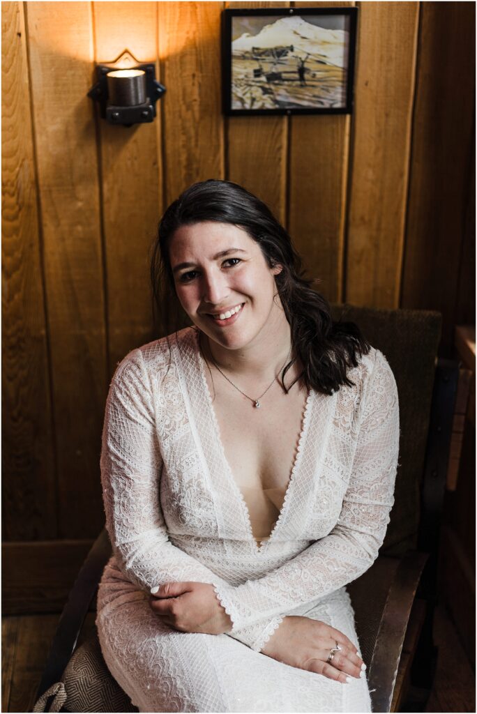 A bride sits on a chair at Timberline's Silcox Hut wearing her white lace wedding gown with plunging neckline. 