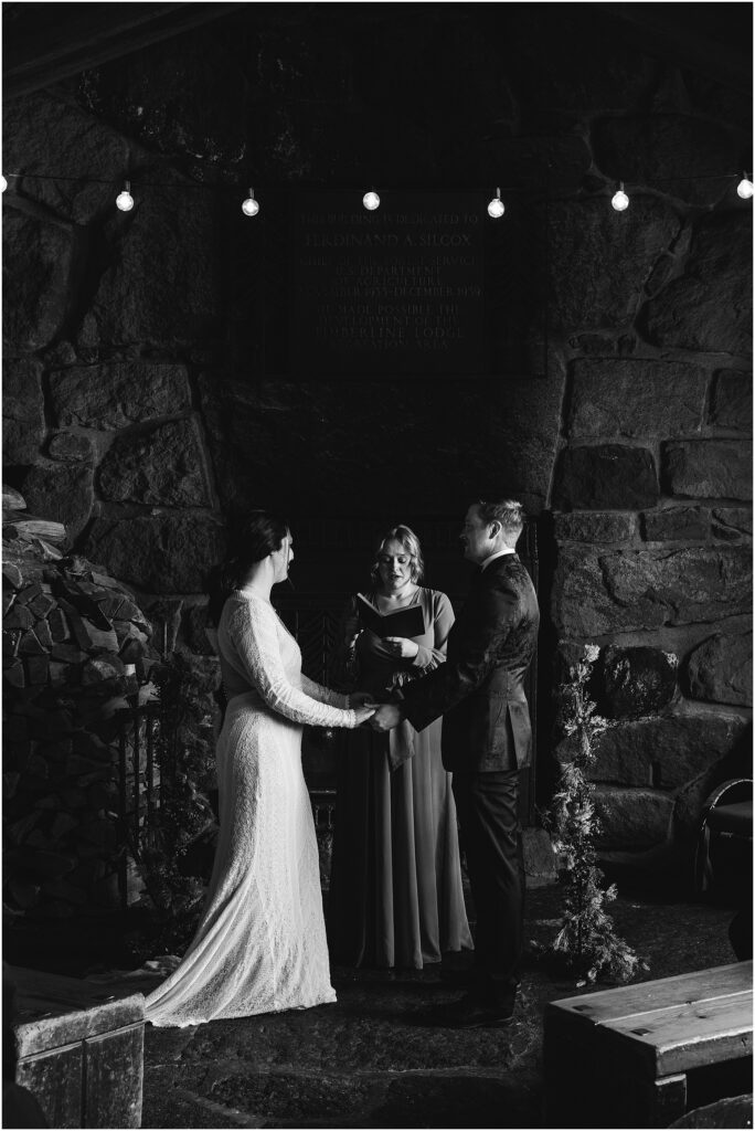 A romantic and moody black and white of a bride and groom holding hands during their vows at the Silcox Hut in Oregon. 