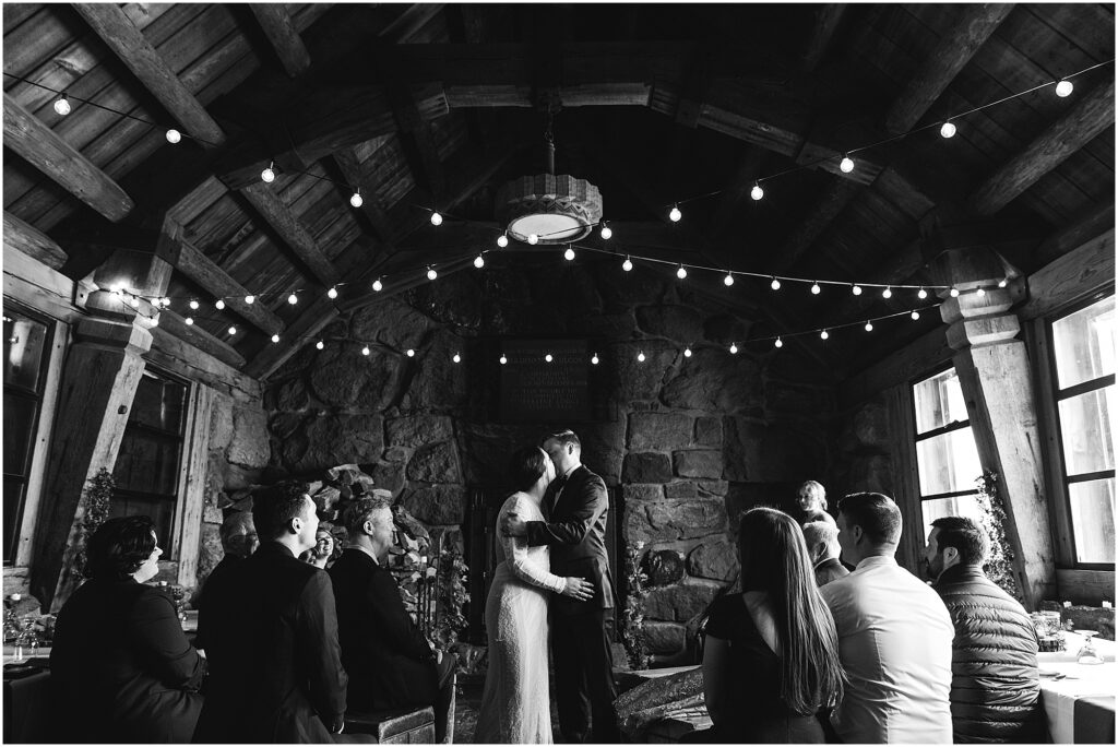 A black and white photo of the bride & groom sharing their first kiss at their Silcox Hut intimate winter wedding ceremony. 