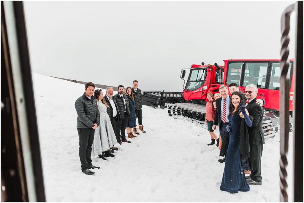 Wedding guests waiting outside in the snow for the bride and groom's skiing sendoff with the bright red snowcat behind them. 