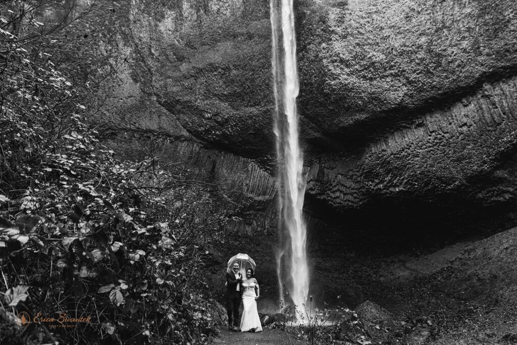 A couple stands near a waterfall base at Columbia River Gorge.