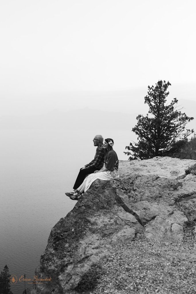 Newlywed couple sits on cliff overlooking Crater Lake.