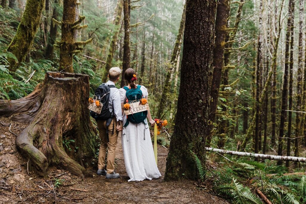 A couple stands with an elopement sign attached to their backpack.