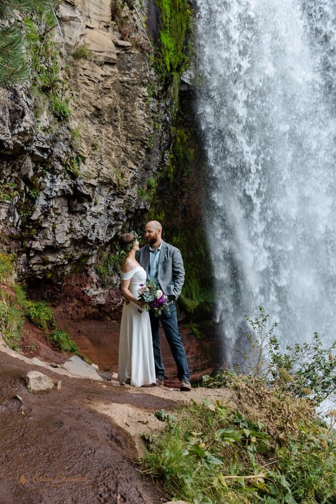 A couple stands near a waterfall for their outdoor wedding in Oregon.