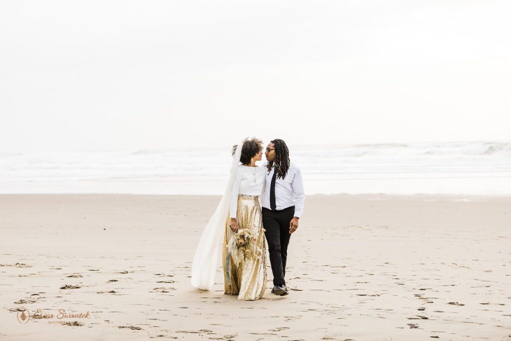 A newlywed couple stands on a beach in Oregon near the shore.