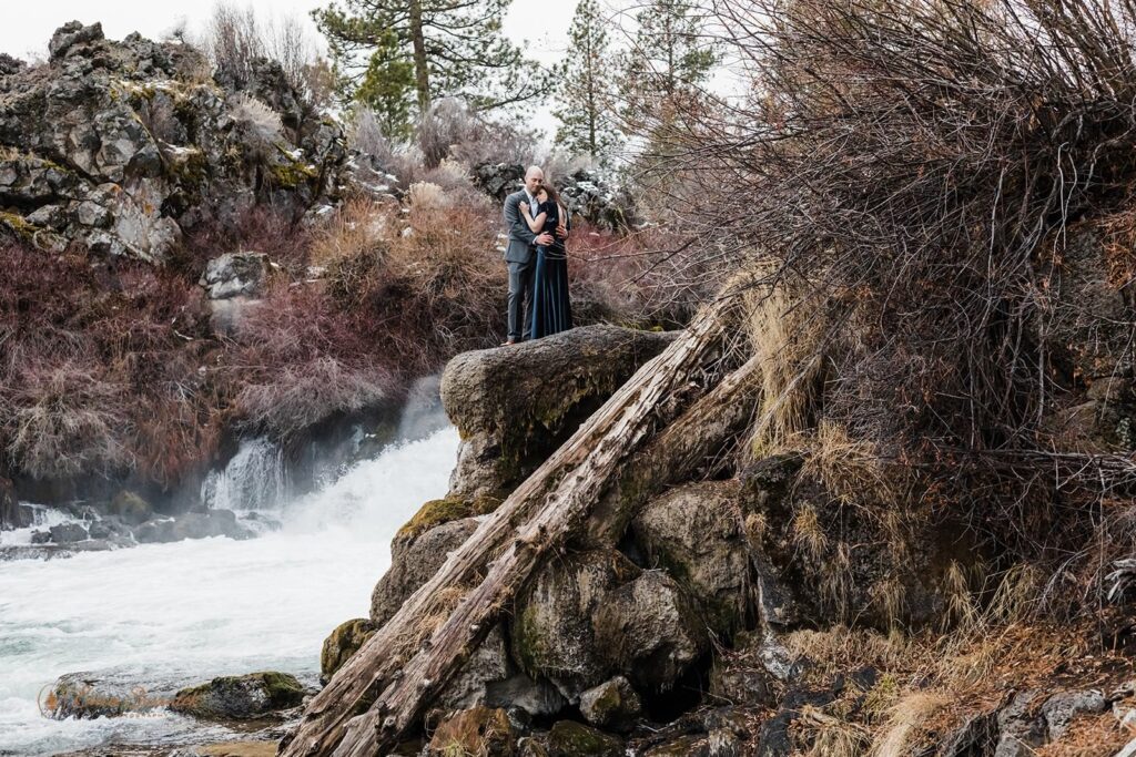 A couple stands near on a cliff's edge near a river in Oregon.
