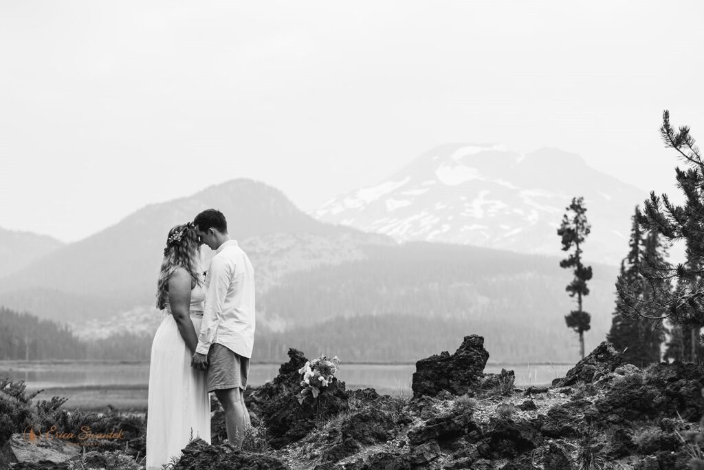 A couple stands near an alpine lake in Oregon and shares a kiss.
