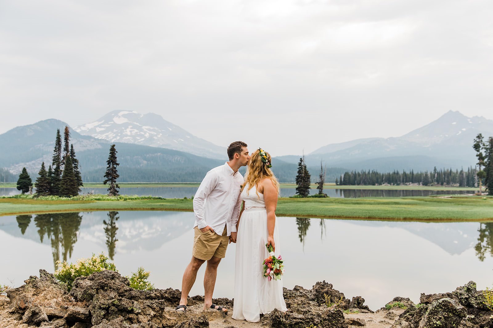 A couple kisses with mountains in the distance during their Central Oregon elopement at Sparks Lake.
