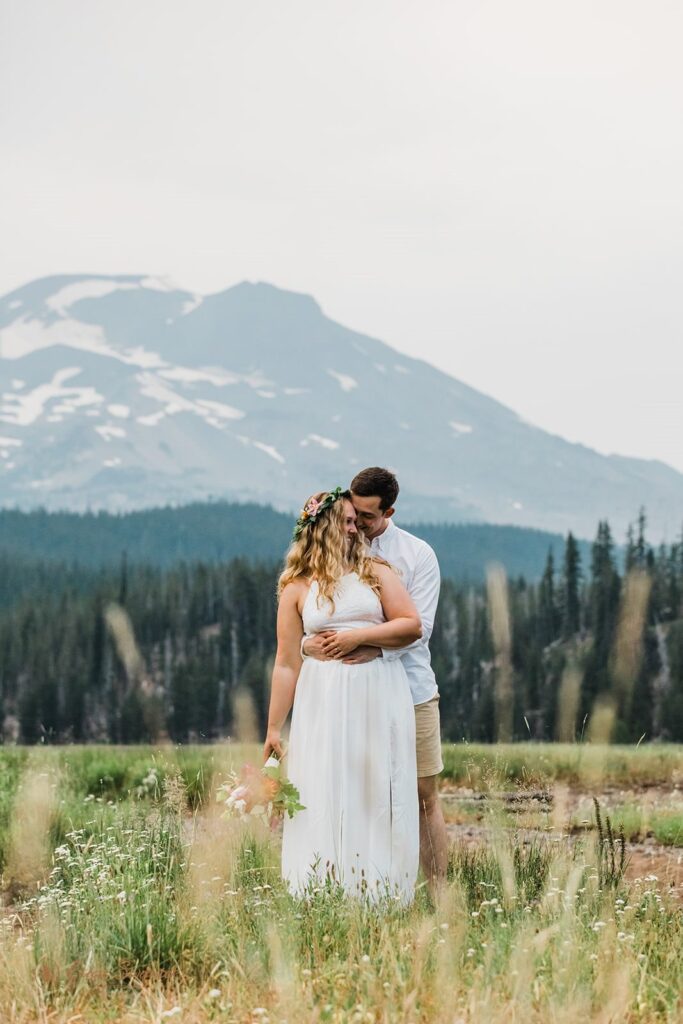 A couple embraces in a meadow amongst tall grass in Oregon.