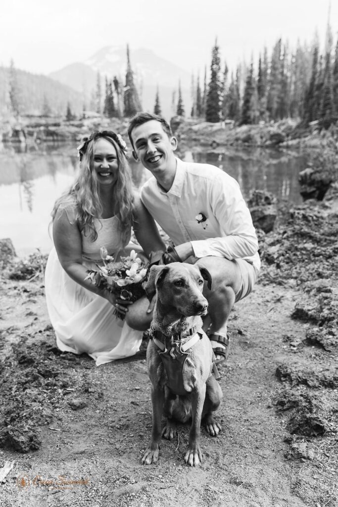 A couple crouches near a lake in Oregon with their dog.