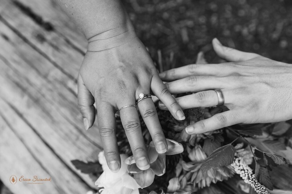 A couple showcases their wedding rings near a bridal bouquet. 