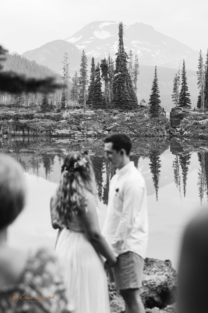A couple holds hands while saying vows near an alpine lake.
