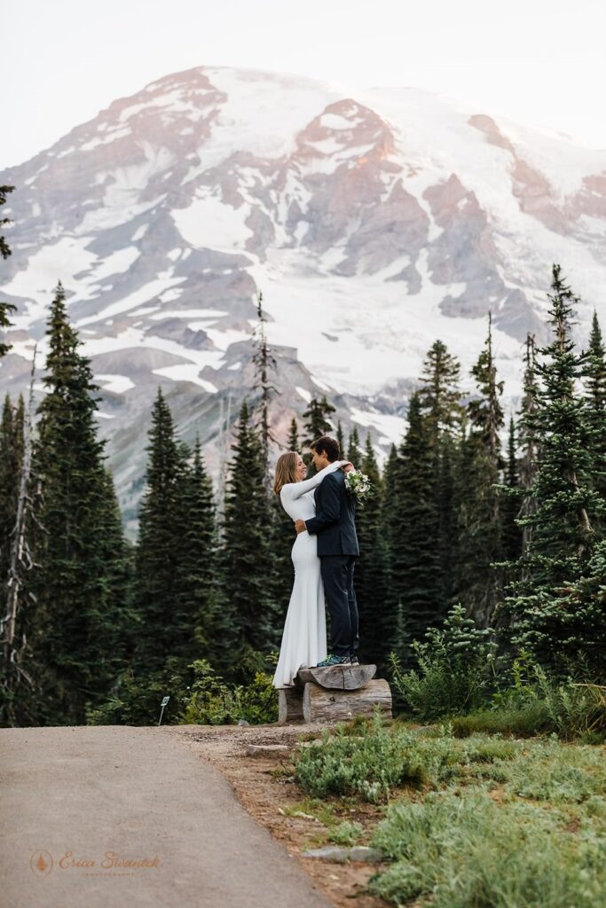 A couple stands on a wooden bench with Mt. Rainier in Washington in the background.