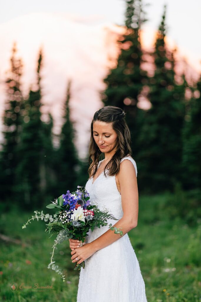 A bride holds a floral bouquet near an evergreen forest.