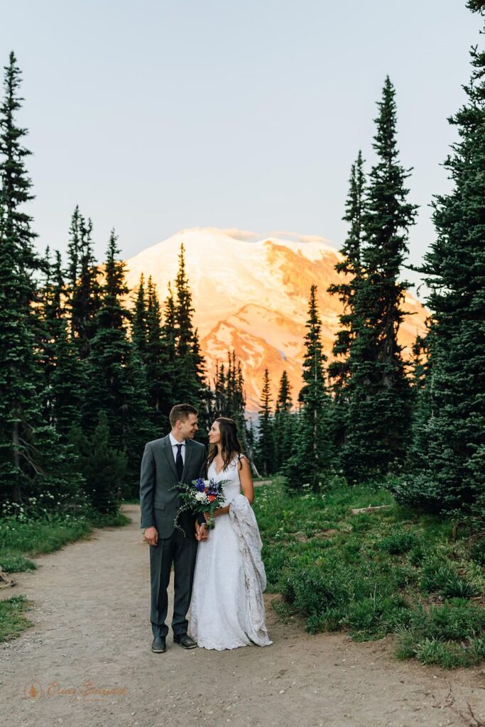 A newlywed couple stands in elopement attire in front of Mt. Rainier.
