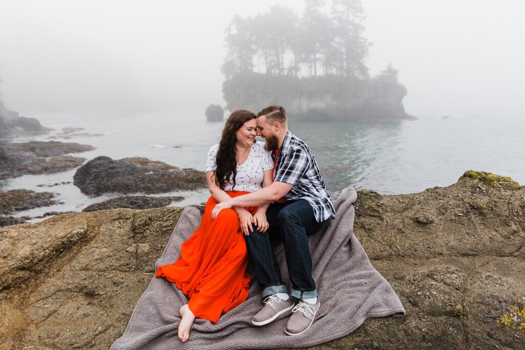 A couple shares laughs while embracing on a blanket on a Pacific Northwest beach.