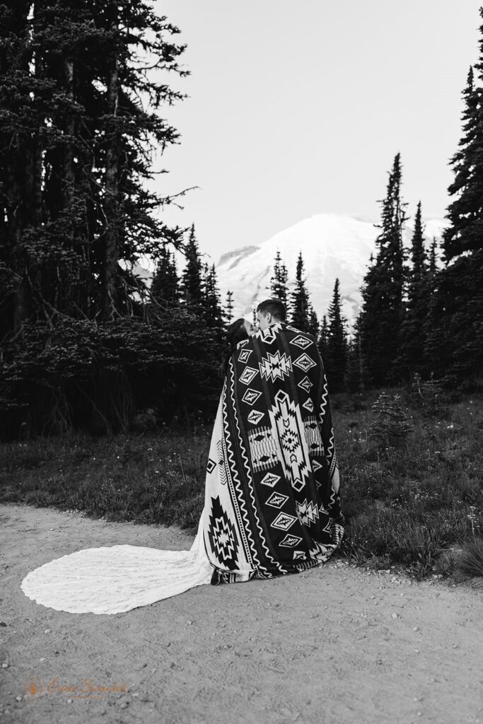 A couple is wrapped in a printed blanket while looking at Mt Rainier in Washington State.