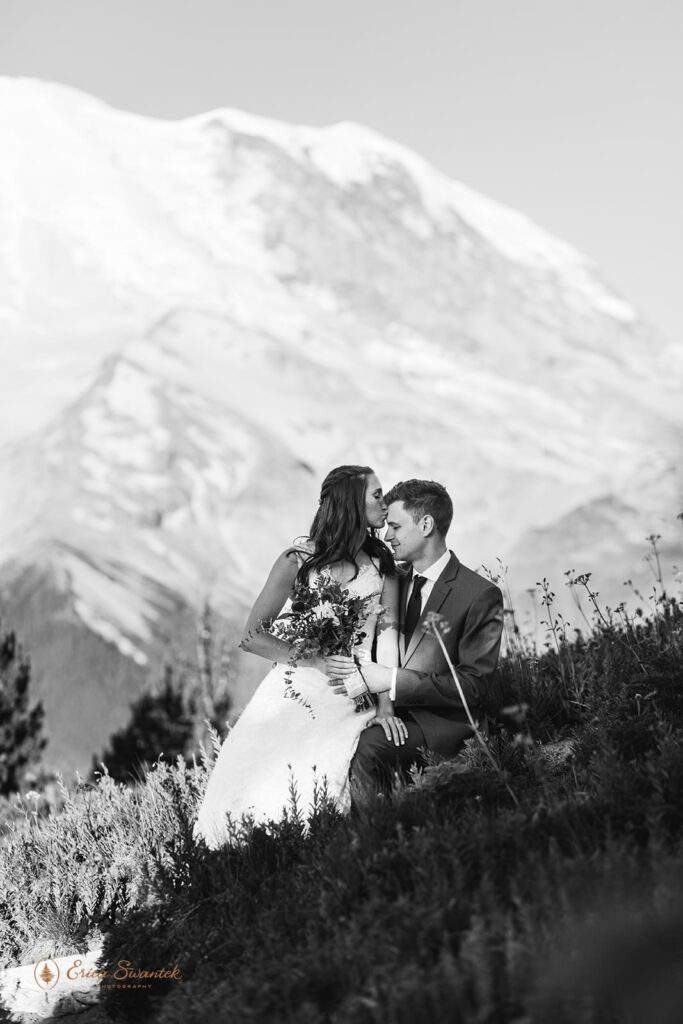 An adventure elopement couple lies in a wildflower meadow by Mt. Rainier. 