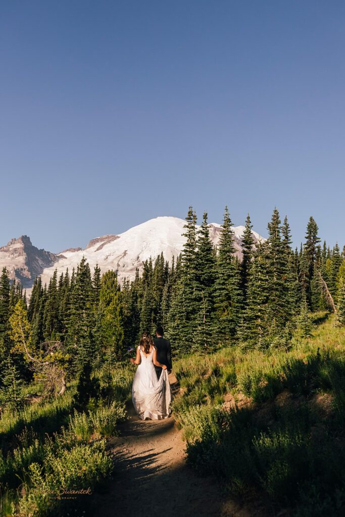 A couple walks along a Mt. Rainier hiking trail while taking Washington State wedding portraits. 