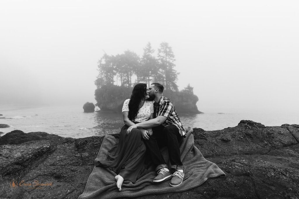 A couple sits on a blanket near the Washington Coast for their engagement photos. 