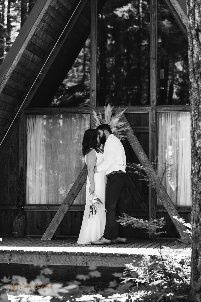 A bride and groom kiss on the porch of a Washington State a-frame cabin. 