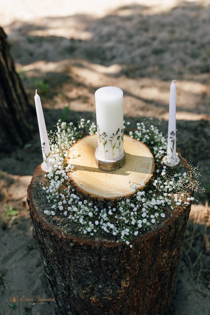 Candles and a floral wreath on a tree stump.