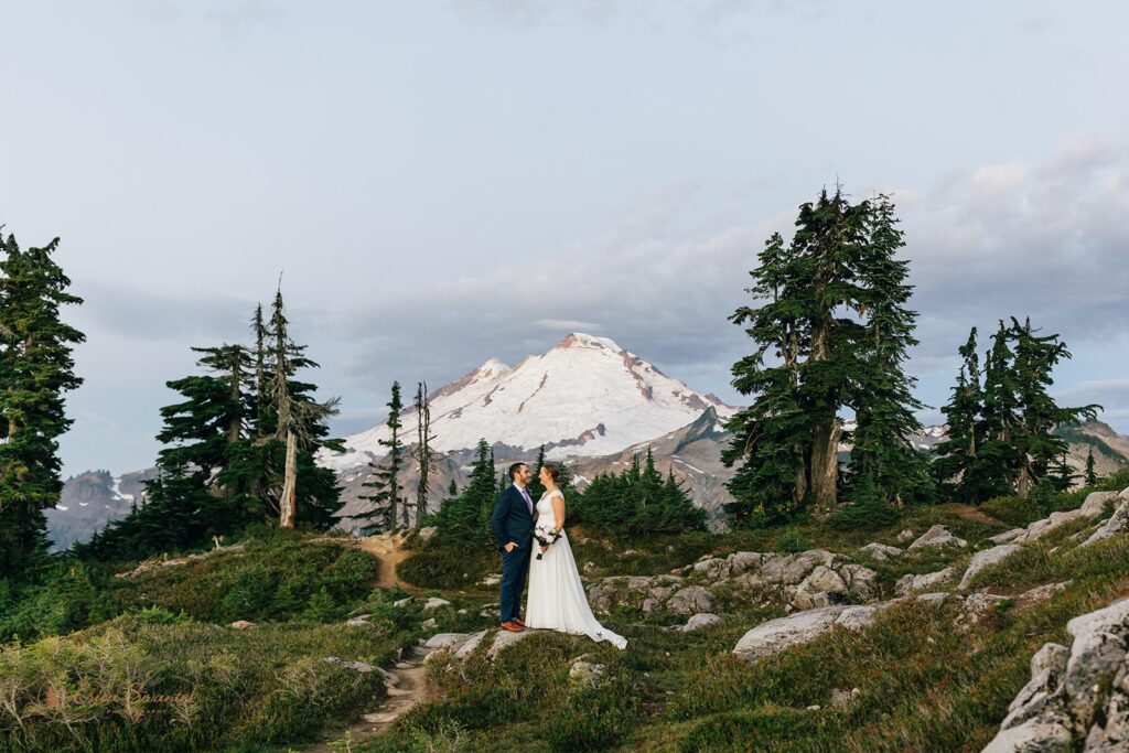 A couple poses in front of a snowy mountain peak in Washington for their elopement.