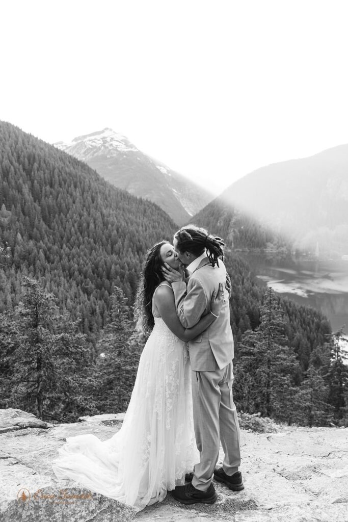 A bride and groom kiss after their wedding vows on an overlook near  mountain peak and lake in Washington. 