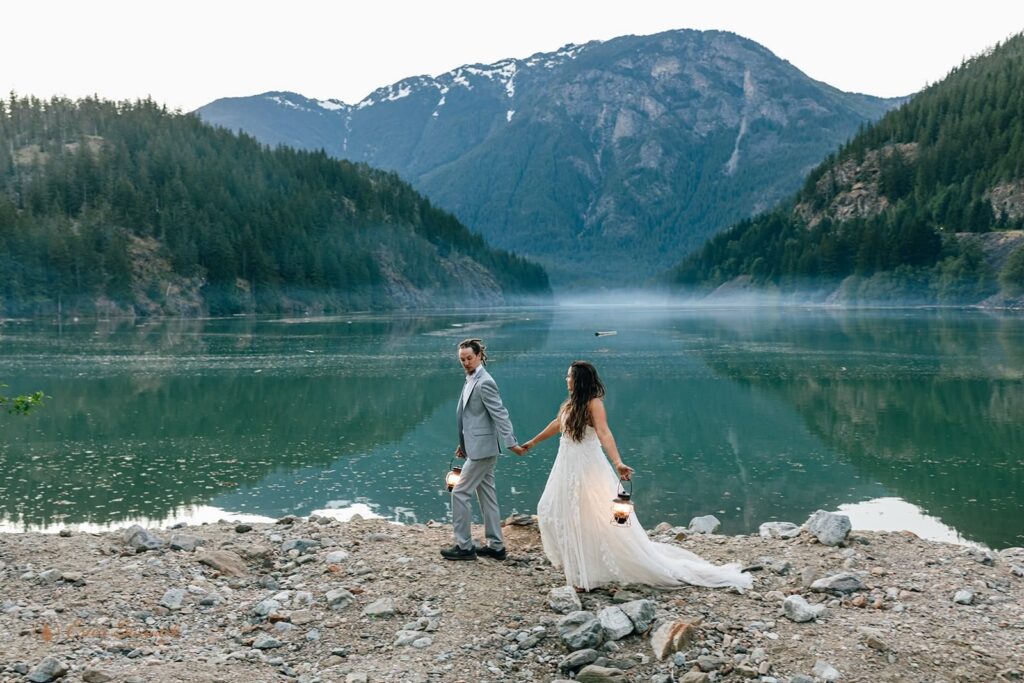 A newlywed couple walks along an alpine lake in Washington State in elopement attire.