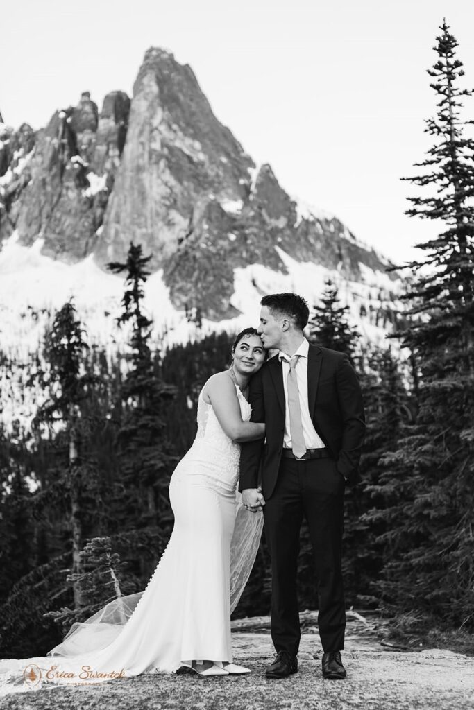 A groom kisses his bride at the base of a Washington mountain peak.