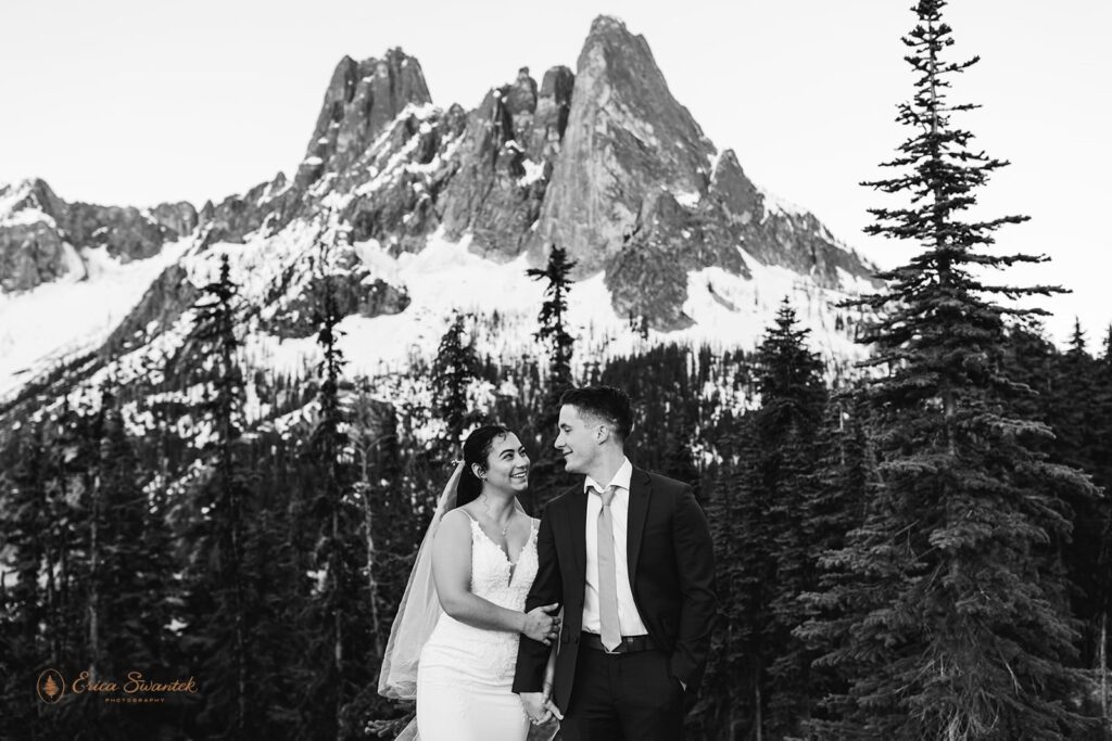 A newlywed couple embraces beneath a snowy mountain peak.