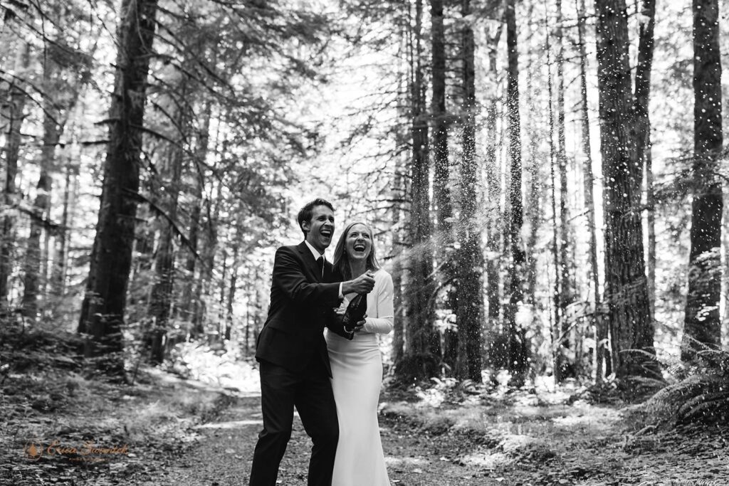 An elopement couple pops champagne during their Washington State forest elopement.