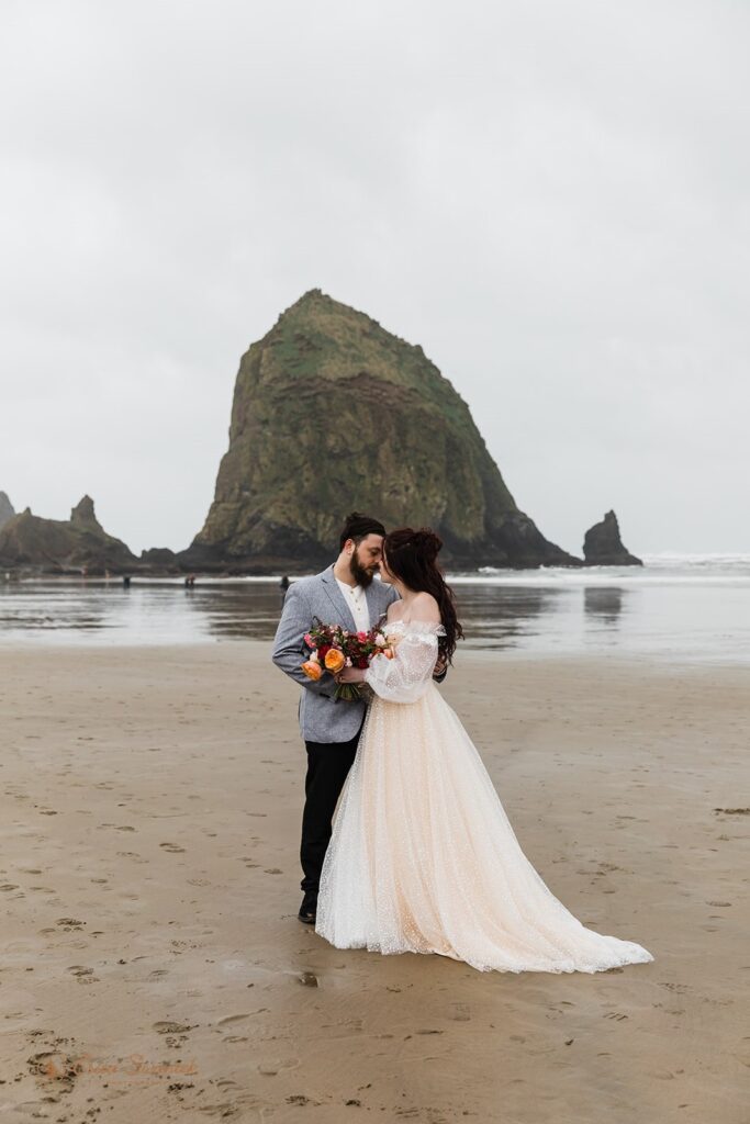 A couple embraces near a large rock formation on Cannon Beach along the Oregon Coast. 