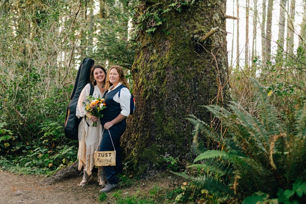 A couple eloping in Oregon stands near a large Sitka spruce in Cape Perpetua Scenic Area. 