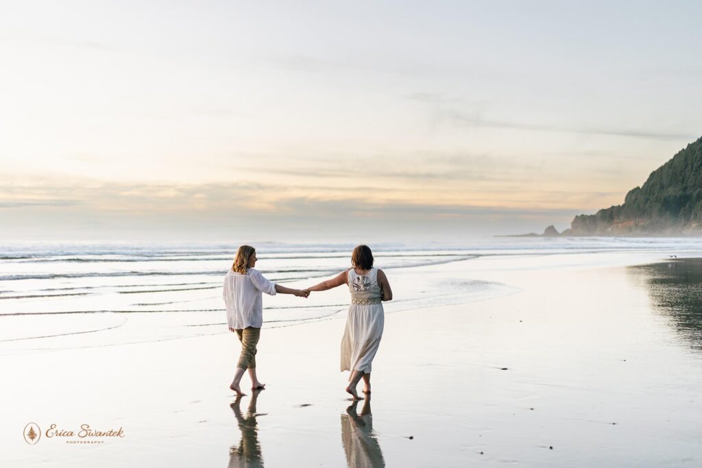 A couple walks hand and hand towards Pacific coast sea cliffs at Neptune Beach in Oregon.