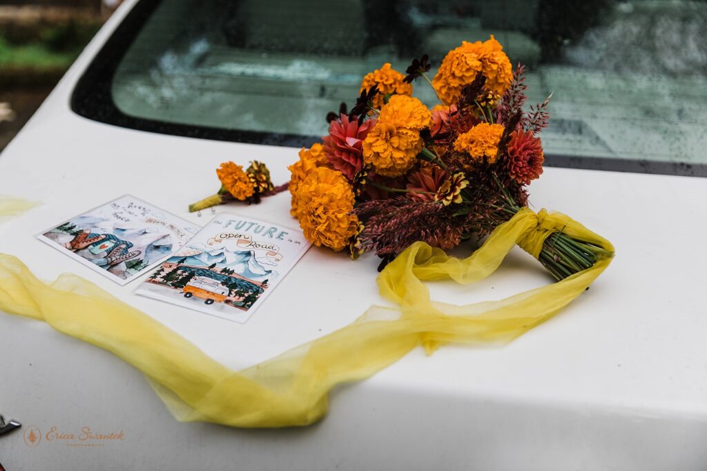 A colorful bridal bouquet sites atop a car trunk with art work. 