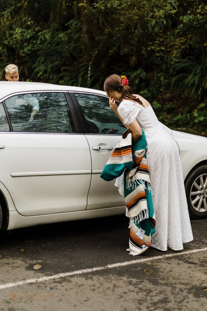 A bride adjusts her hair in the window of a car before a first look in an Oregon forest. 