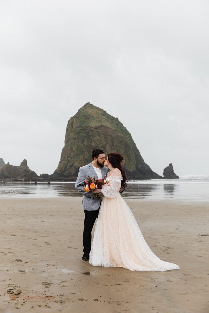 A couple kisses on Cannon Beach  near Haystack Rock during their coastal elopement.