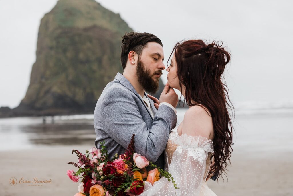 A man holds his bride's chin to go in for a kiss at Cannon Beach during their Oregon Coast elopement
