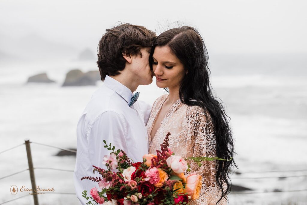 A groom whispers to his bride as they embrace on an overlook during their Oregon Coast elopement.