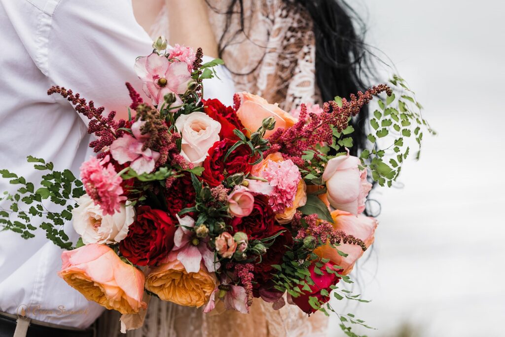 A colorful bridal bouquet with red, pink and orange flowers, filled with greenary.
