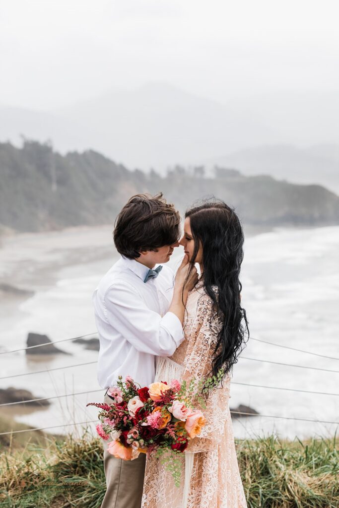 An Oregon Coast elopement couple embraces while wearing neutral, casual wedding attire. 
