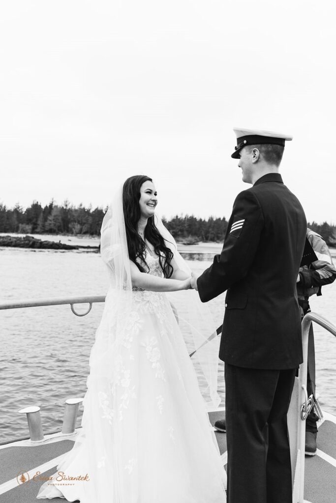 A military couple says wedding vows on a boat while holding hands. 